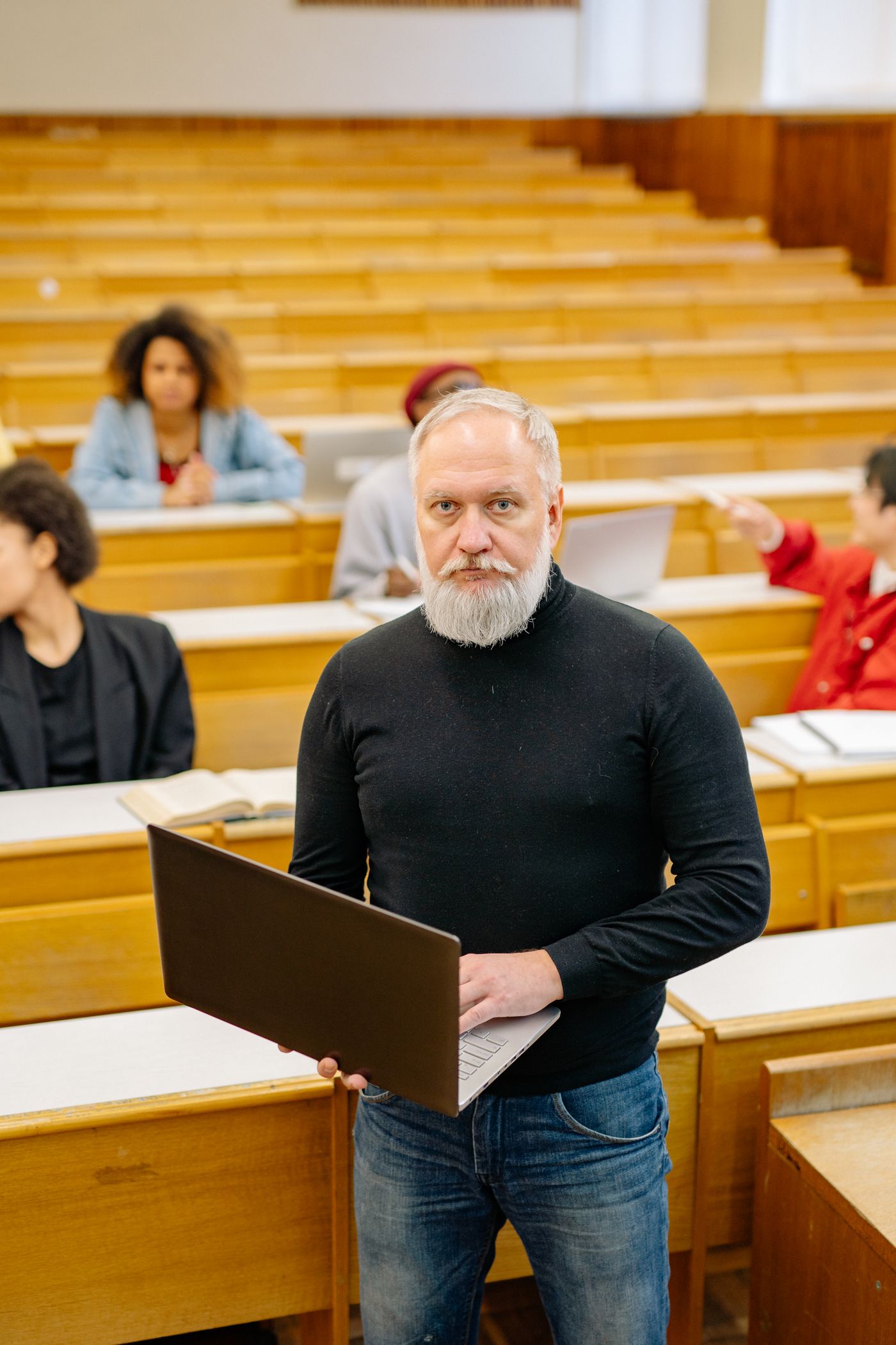 A university professor holding a laptop in a lecture hall