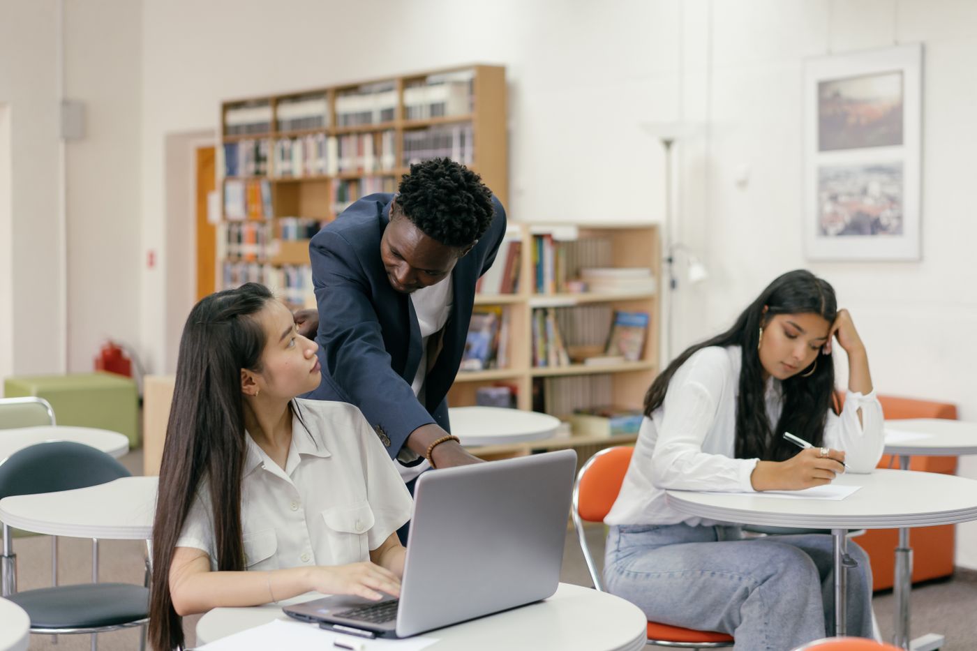 A teacher helping two students at a laptop during a lab
